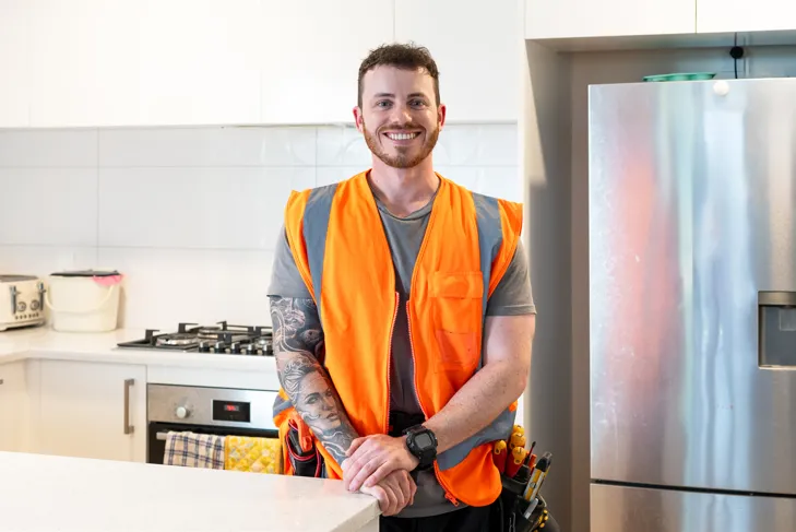 Smiling tradesman wearing a hi-vis vest standing in a modern kitchen